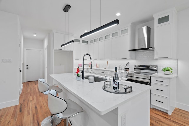 kitchen with stainless steel range with electric stovetop, wall chimney exhaust hood, sink, and an island with sink