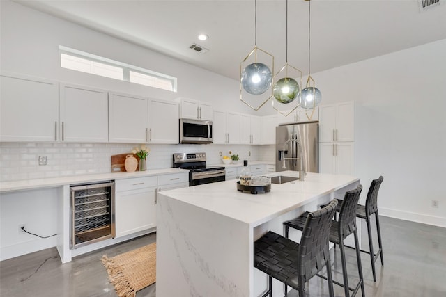 kitchen featuring stainless steel appliances, wine cooler, backsplash, decorative light fixtures, and white cabinets