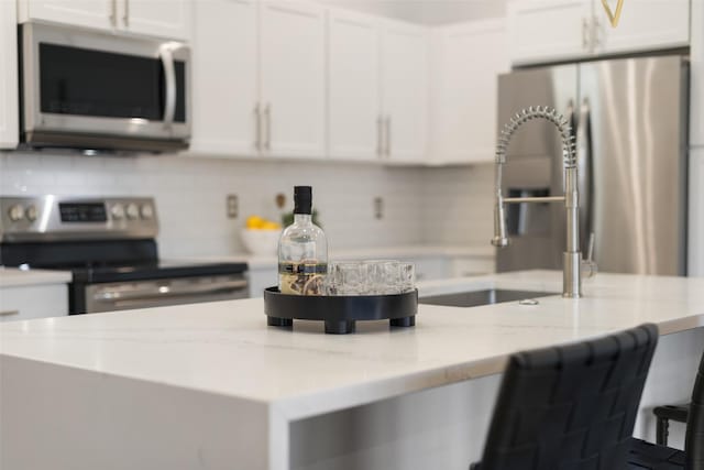 kitchen featuring light stone counters, a breakfast bar, white cabinets, and stainless steel appliances