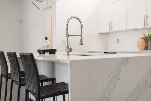 bar with tasteful backsplash, white cabinetry, and sink