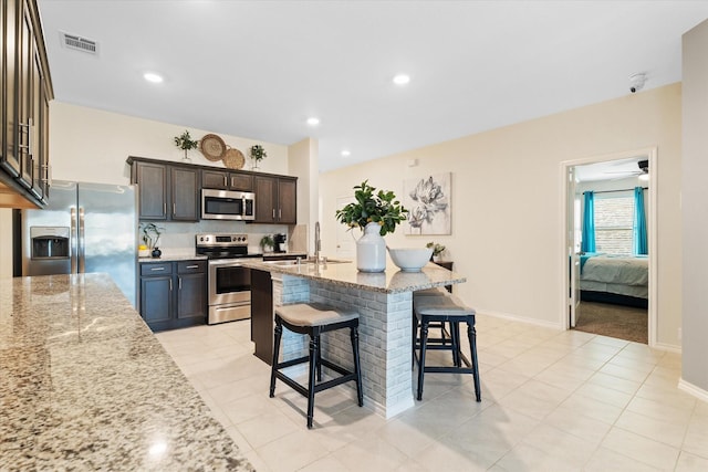 kitchen with light stone counters, stainless steel appliances, a kitchen breakfast bar, and dark brown cabinets