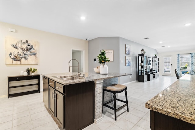 kitchen with light stone counters, sink, light tile patterned floors, and a center island with sink