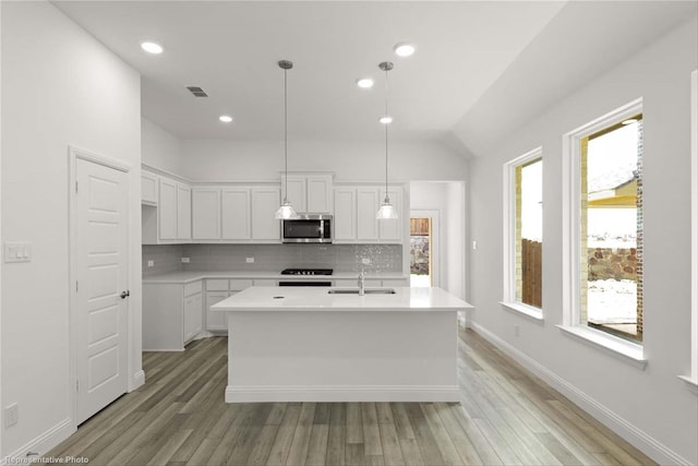 kitchen with white cabinets, pendant lighting, range, and an island with sink