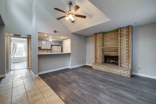 unfurnished living room featuring a brick fireplace, a textured ceiling, ceiling fan, high vaulted ceiling, and tile patterned flooring