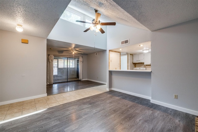 unfurnished living room featuring a textured ceiling, hardwood / wood-style flooring, high vaulted ceiling, and ceiling fan