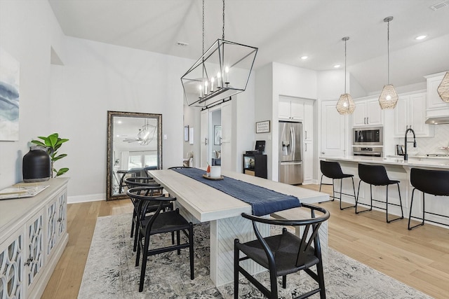 dining space featuring light hardwood / wood-style flooring, ceiling fan with notable chandelier, and sink