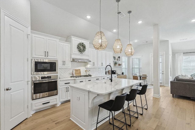 kitchen with stainless steel appliances, an island with sink, decorative light fixtures, a kitchen bar, and white cabinets