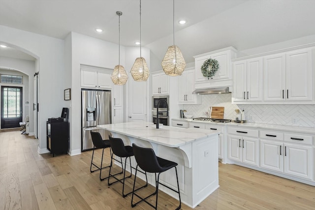 kitchen featuring stainless steel appliances, vaulted ceiling, a kitchen island with sink, and white cabinetry