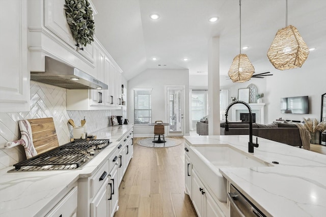 kitchen with sink, a brick fireplace, light stone counters, decorative light fixtures, and white cabinets