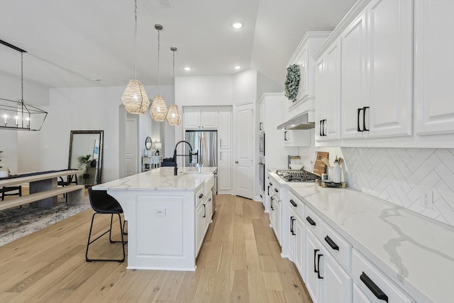 kitchen with pendant lighting, backsplash, white cabinets, an island with sink, and light stone counters