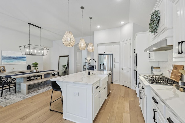 kitchen featuring light stone counters, a center island with sink, white cabinets, and pendant lighting