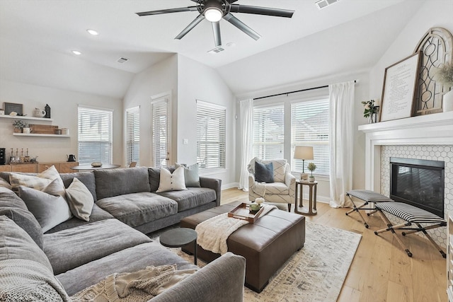 living room with lofted ceiling, a healthy amount of sunlight, light wood-type flooring, and a tile fireplace