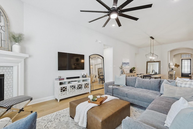 living room featuring a tile fireplace, light hardwood / wood-style flooring, and ceiling fan with notable chandelier