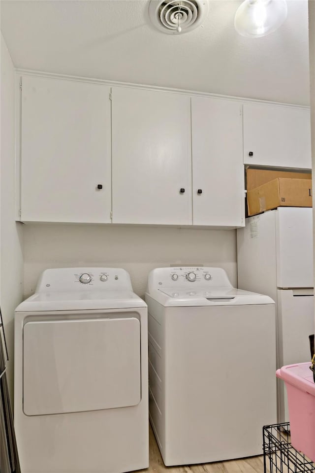 laundry area featuring cabinets, washer and dryer, and light hardwood / wood-style flooring