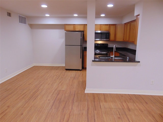 kitchen with appliances with stainless steel finishes, kitchen peninsula, sink, and light hardwood / wood-style flooring