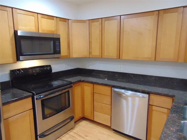 kitchen with dark stone countertops, light hardwood / wood-style flooring, and appliances with stainless steel finishes