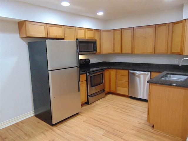 kitchen featuring appliances with stainless steel finishes, light hardwood / wood-style floors, sink, and dark stone countertops