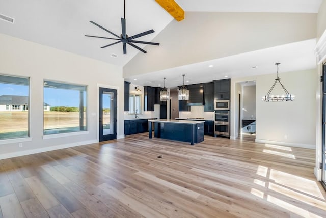 kitchen featuring appliances with stainless steel finishes, beam ceiling, a center island, hanging light fixtures, and a breakfast bar area