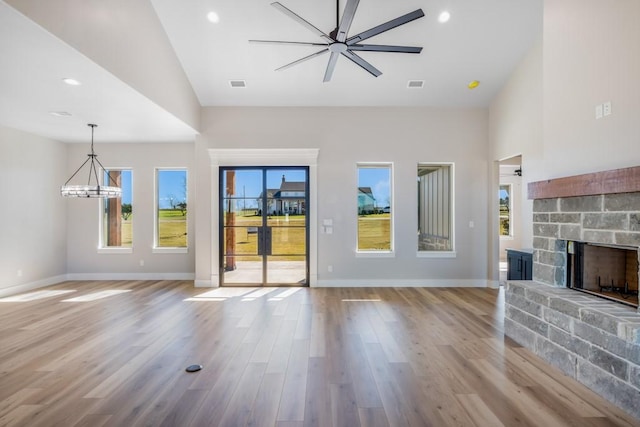 unfurnished living room featuring a fireplace, high vaulted ceiling, ceiling fan with notable chandelier, and light hardwood / wood-style flooring