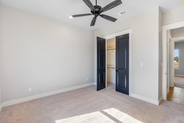 unfurnished bedroom with a spacious closet, light colored carpet, ceiling fan, and a closet