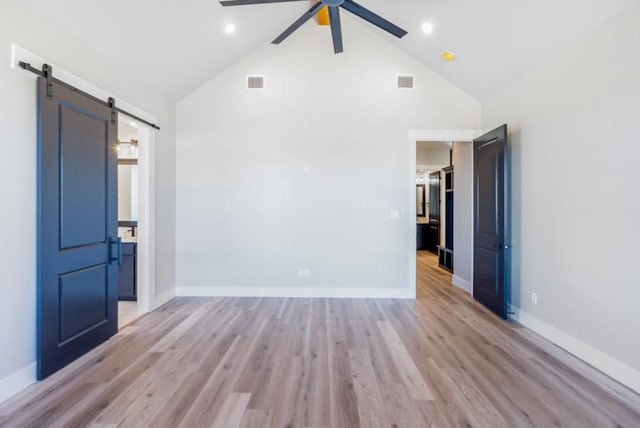 spare room featuring a barn door, ceiling fan, light hardwood / wood-style flooring, and vaulted ceiling