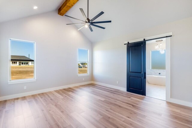 unfurnished bedroom with ensuite bathroom, a barn door, lofted ceiling with beams, and light hardwood / wood-style flooring