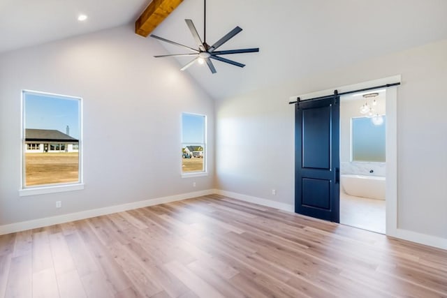 unfurnished bedroom with connected bathroom, high vaulted ceiling, beam ceiling, a barn door, and light wood-type flooring