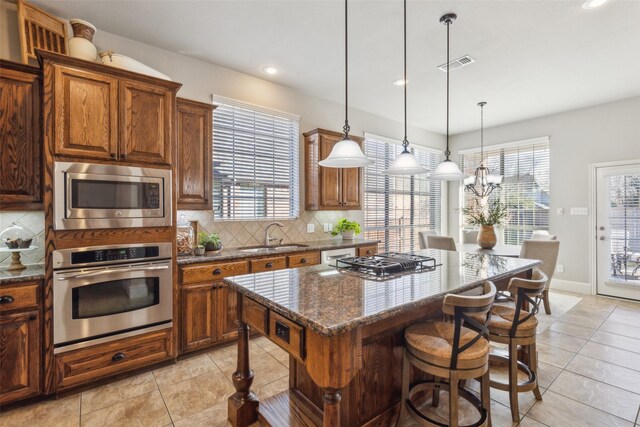 kitchen with appliances with stainless steel finishes, sink, dark stone countertops, a kitchen island, and hanging light fixtures