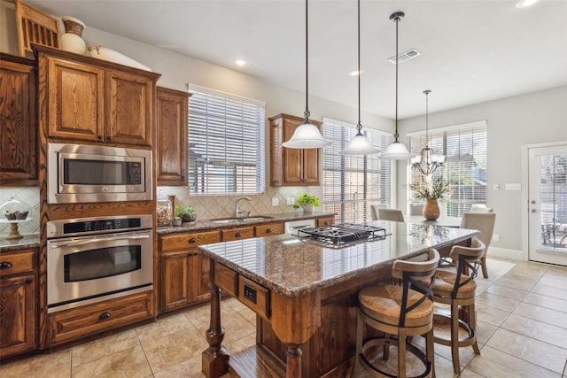 kitchen with pendant lighting, a center island, stainless steel appliances, dark stone counters, and sink