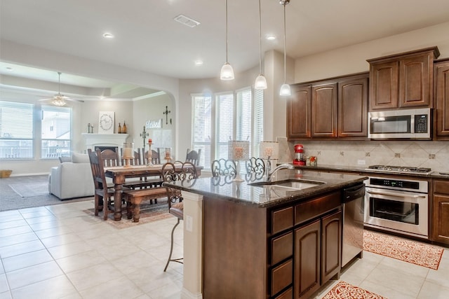 kitchen featuring sink, dark stone countertops, hanging light fixtures, stainless steel appliances, and a center island with sink