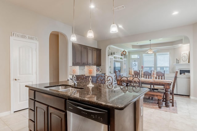 kitchen with dishwasher, sink, dark stone countertops, a kitchen island with sink, and dark brown cabinets