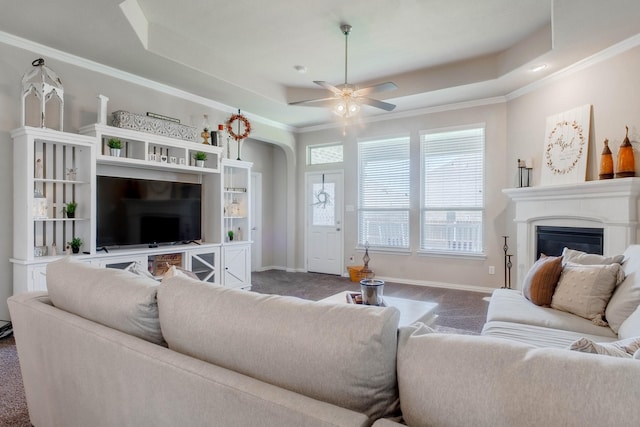 living room featuring dark colored carpet, ceiling fan, ornamental molding, and a tray ceiling