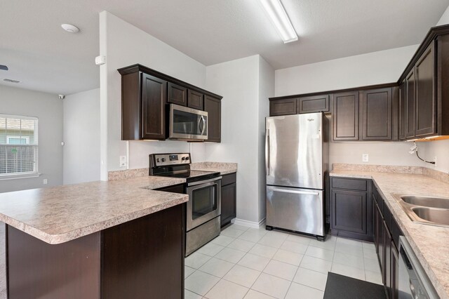 kitchen with dark brown cabinetry, sink, kitchen peninsula, light tile patterned floors, and appliances with stainless steel finishes