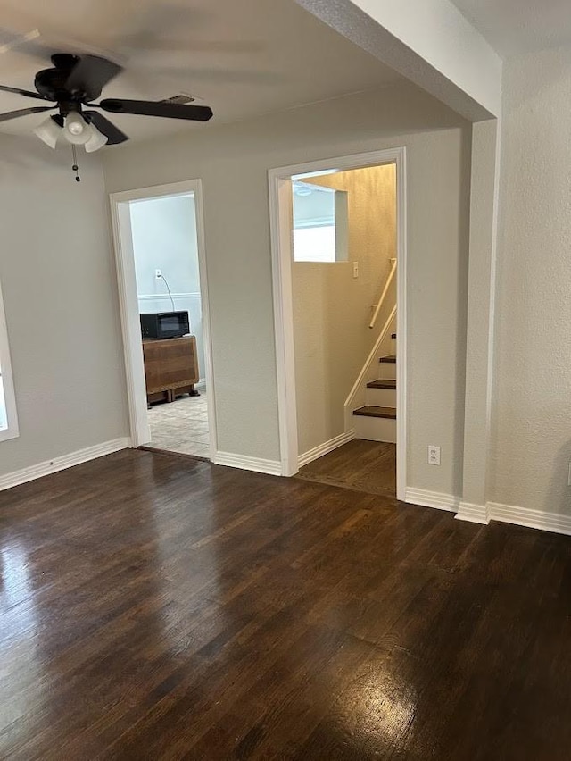 unfurnished living room with stairs, dark wood-style floors, baseboards, and ceiling fan