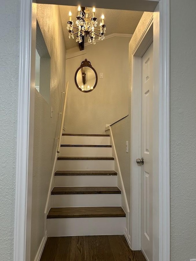 stairway with a notable chandelier, lofted ceiling, a textured wall, and wood finished floors