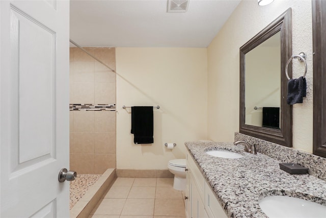 bathroom with tile patterned floors, vanity, tiled shower, and toilet