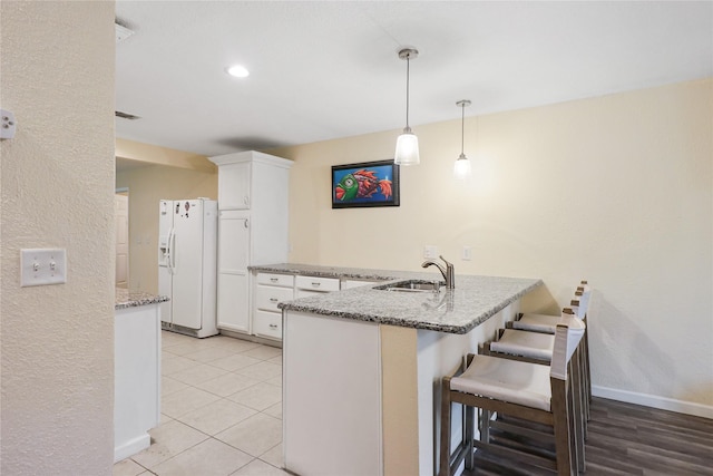 kitchen with kitchen peninsula, hanging light fixtures, white cabinetry, white fridge with ice dispenser, and a breakfast bar area