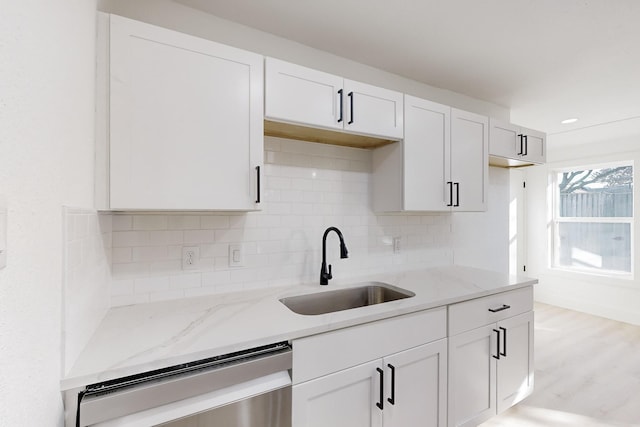 kitchen with backsplash, light stone counters, sink, dishwasher, and white cabinetry