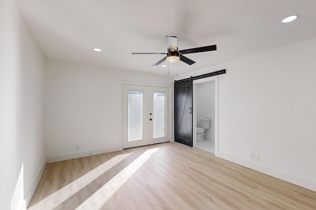 unfurnished bedroom with ceiling fan, french doors, a barn door, ensuite bathroom, and light hardwood / wood-style floors