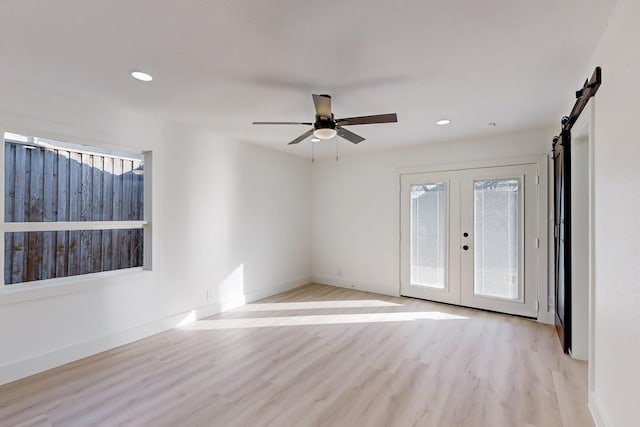 unfurnished room with a barn door, ceiling fan, french doors, and light hardwood / wood-style flooring