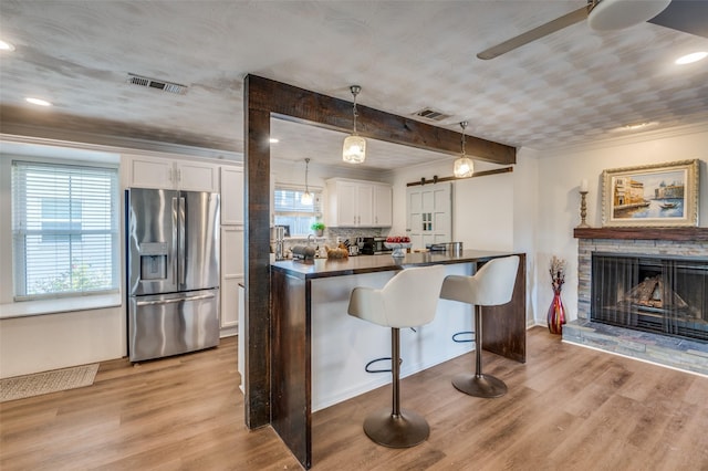 kitchen with stainless steel refrigerator with ice dispenser, light hardwood / wood-style floors, decorative light fixtures, a breakfast bar, and white cabinets