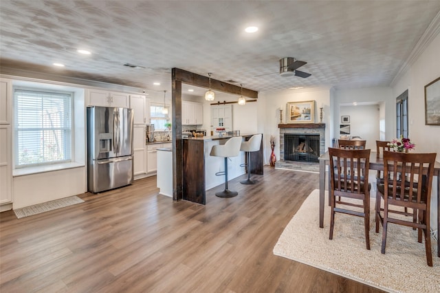 dining space featuring a fireplace, light hardwood / wood-style flooring, ceiling fan, and ornamental molding