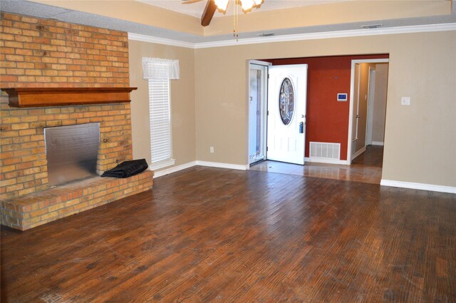 unfurnished living room with ceiling fan, ornamental molding, a fireplace, a tray ceiling, and dark hardwood / wood-style flooring