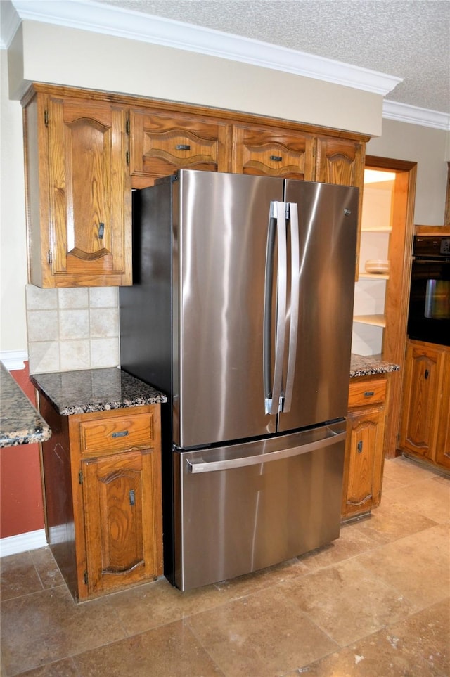 kitchen featuring crown molding, stainless steel fridge, dark stone countertops, tasteful backsplash, and oven