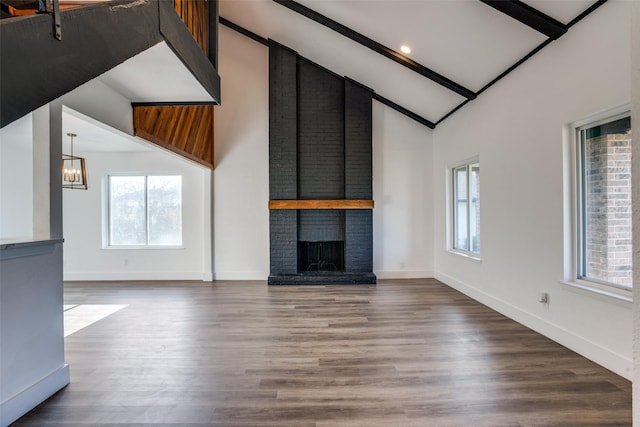 unfurnished living room featuring an inviting chandelier, wood-type flooring, a brick fireplace, and vaulted ceiling with beams