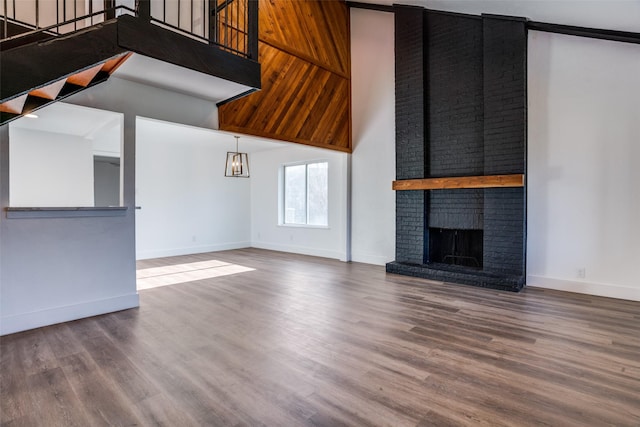 unfurnished living room with a towering ceiling, wood-type flooring, and a brick fireplace