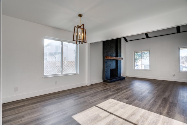 unfurnished living room with an inviting chandelier, beam ceiling, dark wood-type flooring, and a brick fireplace