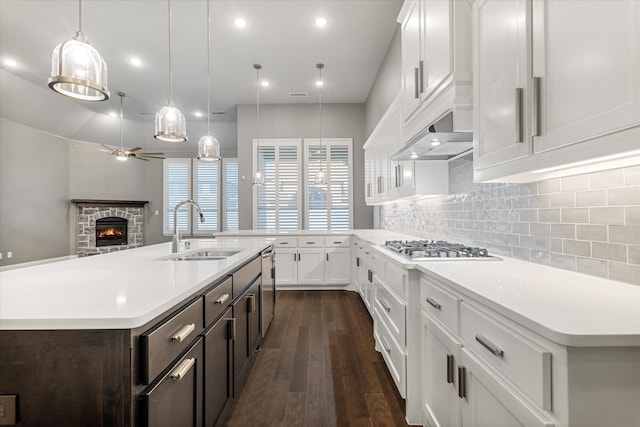 kitchen with a stone fireplace, a kitchen island with sink, sink, and white cabinets