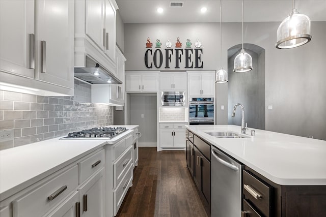 kitchen with a sink, stainless steel appliances, wall chimney exhaust hood, light countertops, and dark wood finished floors