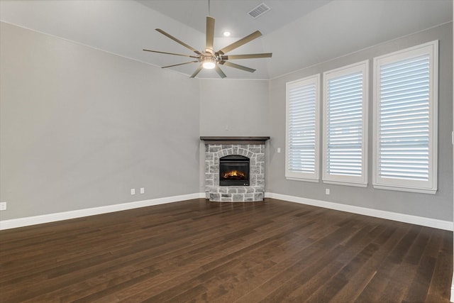 unfurnished living room with ceiling fan, dark wood-type flooring, visible vents, a stone fireplace, and baseboards